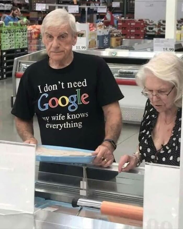 Elderly man wearing a funny marriage meme shirt about his wife knowing everything while shopping with his spouse.