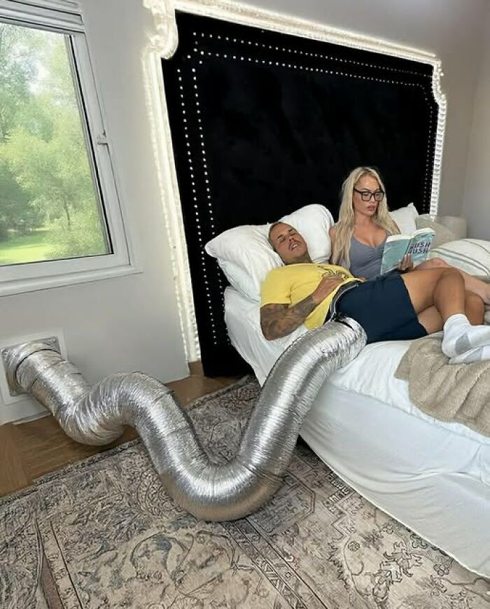 Couple in bed with husband humorously connected to a vent pipe, illustrating funny and chaotic marriage memes.
