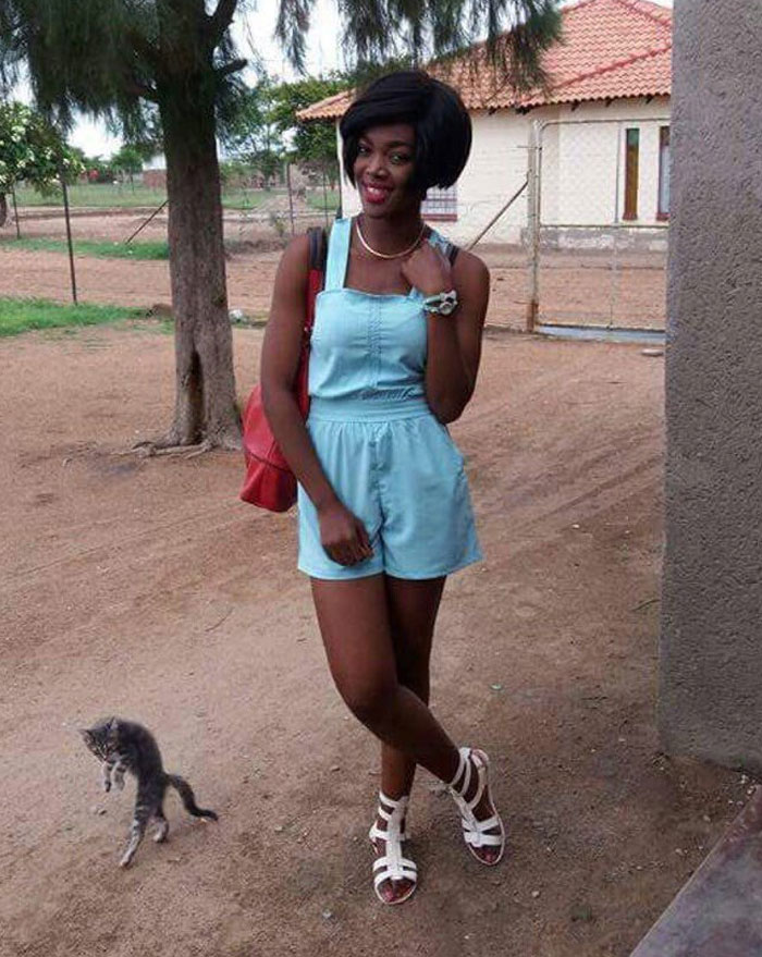 Woman in blue romper posing outside while a pet cat crashes the photo by jumping nearby, adding a funny moment.
