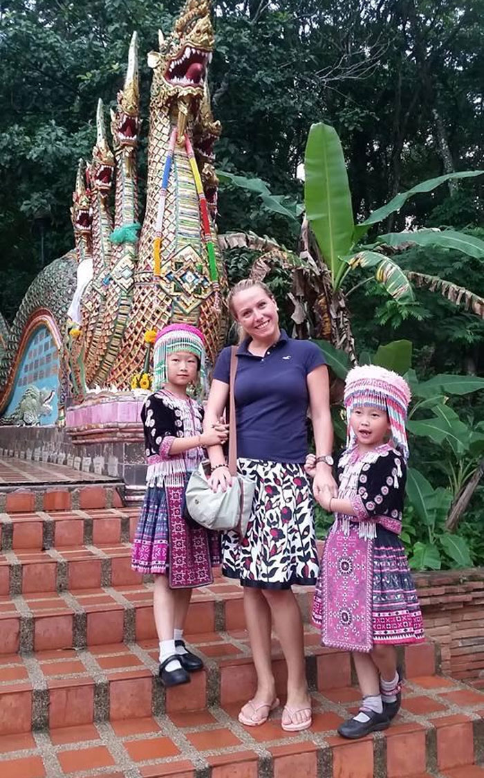 Woman posing with two children in traditional dress by ornate dragon statue on vacation, capturing funny vacation pics.