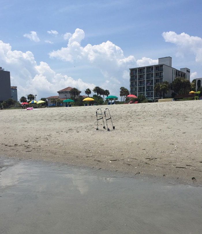 A walker standing alone on a sandy beach with colorful umbrellas and buildings in the background, a funny vacation pic.