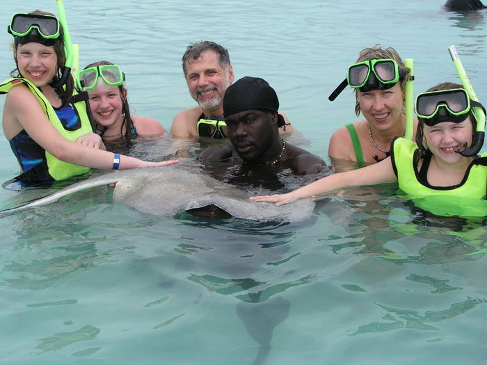 Group of people in snorkeling gear touching a stingray in shallow water during a funny vacation pic moment