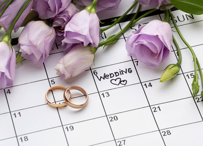 Calendar with wedding plans marked, two wedding rings, and purple flowers symbolizing bride cuts mom off key wedding plans. Calendar with wedding plans marked, two wedding rings, and purple flowers symbolizing bride cuts mom off key wedding plans.