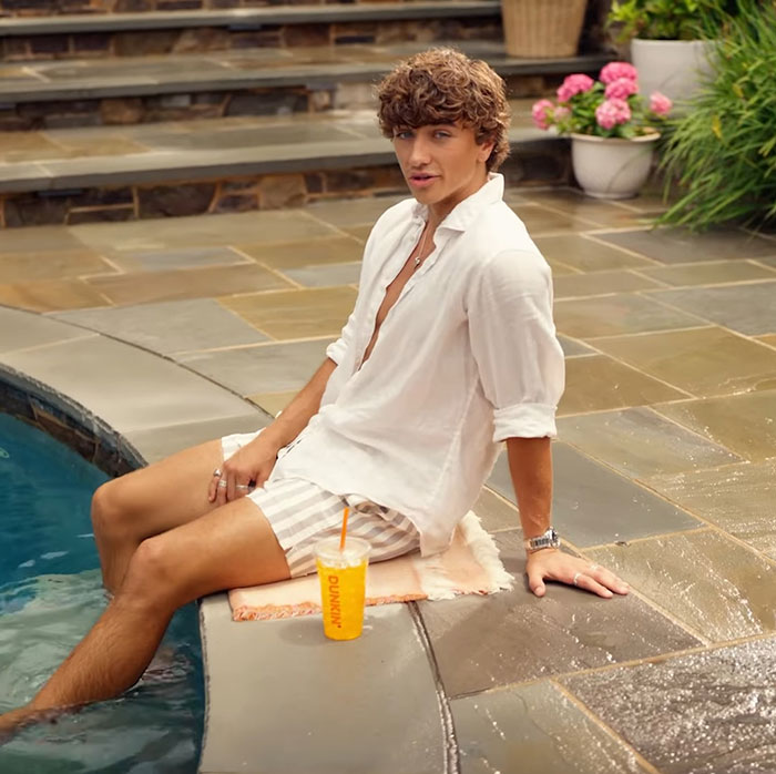 Young man sitting by a pool wearing a white shirt and striped shorts, related to genetics and woke outrage discussion. Young man sitting by a pool wearing a white shirt and striped shorts, related to genetics and woke outrage discussion.