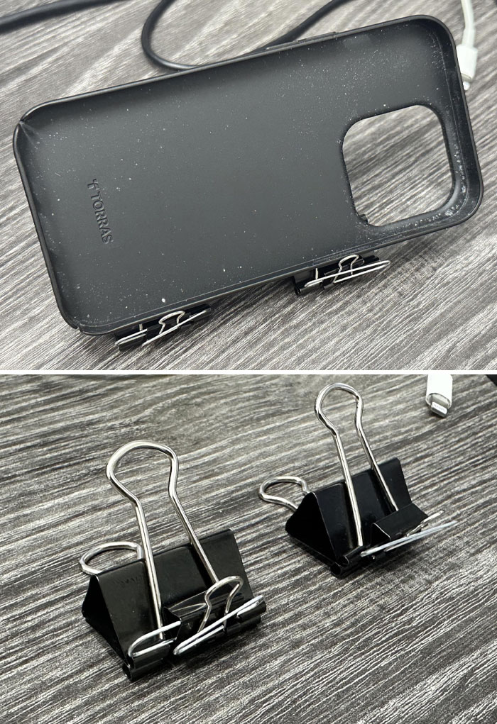 Black phone case held upright by binder clips on desk, demonstrating genius life hacks with everyday office supplies.
