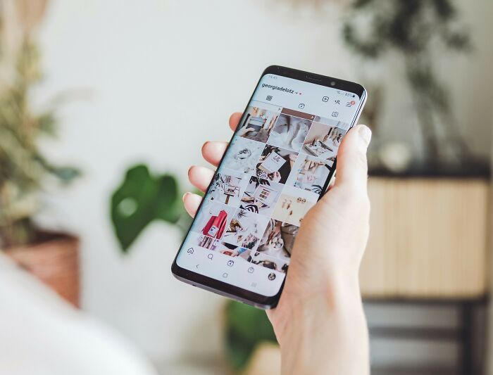Person holding smartphone browsing social media, representing unhinged hacks done to land job techniques.