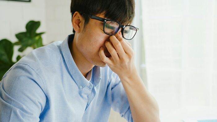 Young man wearing glasses sitting indoors looking stressed, illustrating downsides of having a dog as a pet.