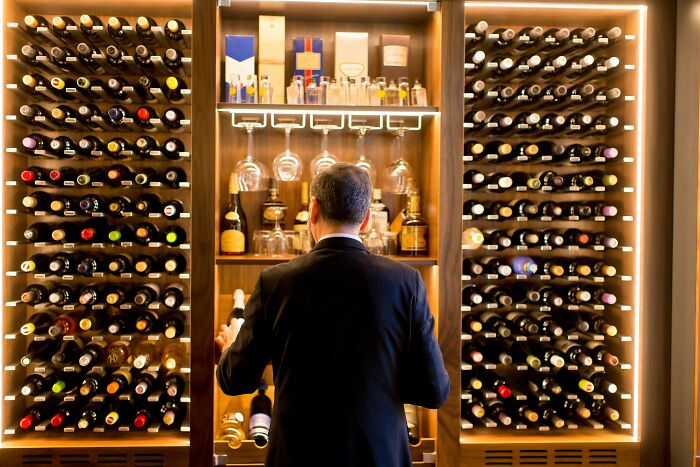 Man in suit selects expensive wine from a large, well-lit wine collection showcasing the wealth gap perspective.
