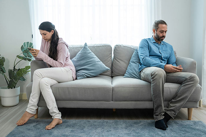 Man and wife sitting apart on couch looking upset, illustrating conflict over bonus stepdaughter and quiet family life.