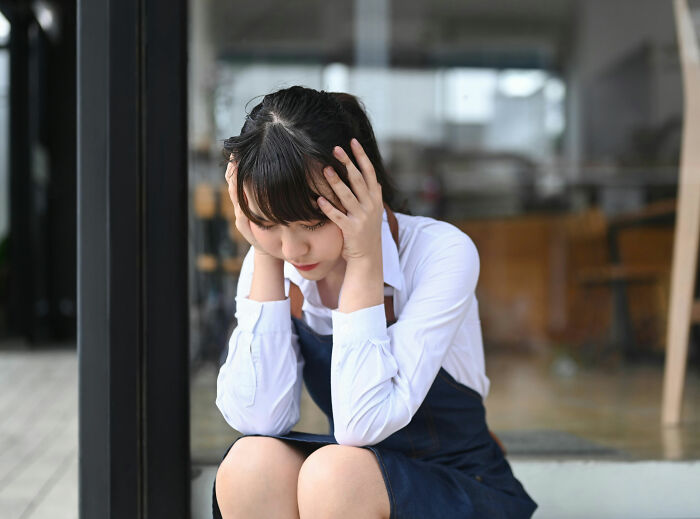 Young woman sitting with head in hands, illustrating celebs trying to be relatable but showing how out-of-touch they are.