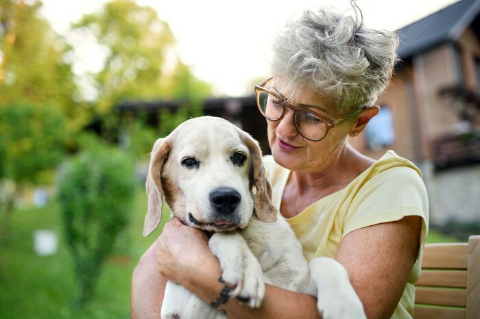 Older woman with glasses hugging a white dog outdoors, illustrating the challenges of having a dog as a pet.