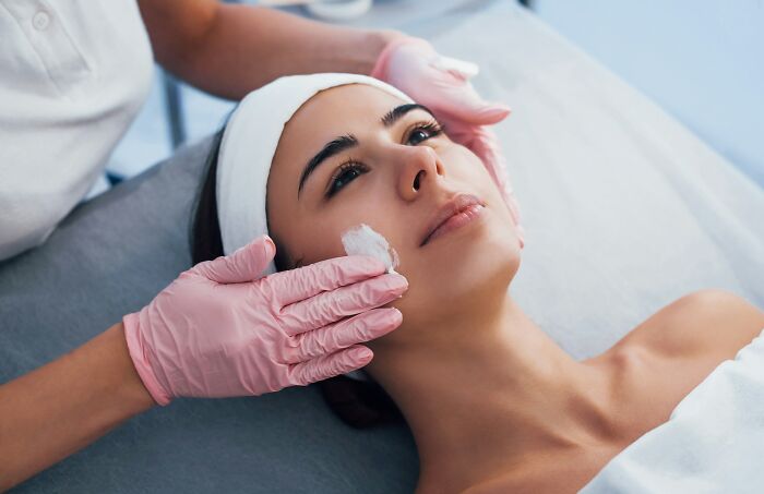 Woman receiving facial treatment at a spa with gloves on hands, relating to shopping and self-care relaxation.