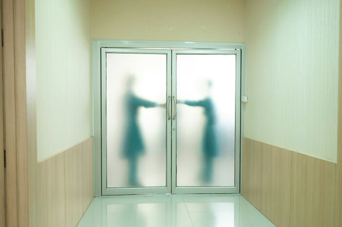 Blurred figures appearing through frosted glass doors in a dim hallway, evoking chilling paranormal encounters of night shift workers.