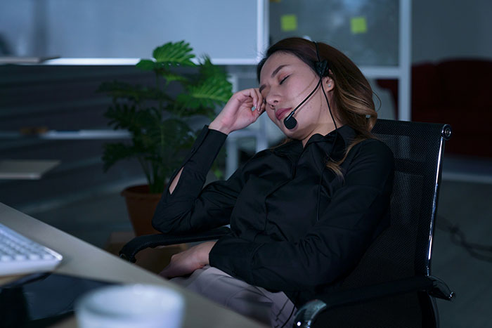 Tired woman wearing headset sitting at desk in dark office, reflecting quiet life with two kids and bonus stepdaughter conflict.