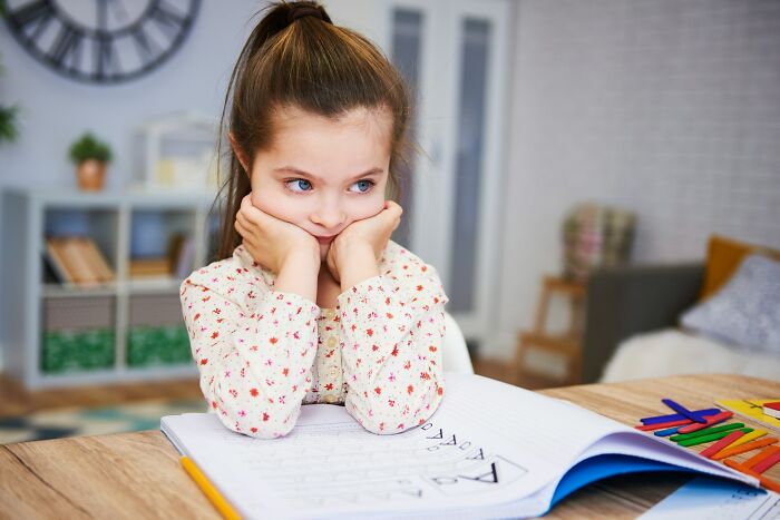 Young girl looking puzzled while sitting at a table with an open notebook, representing glitches in the matrix experiences.