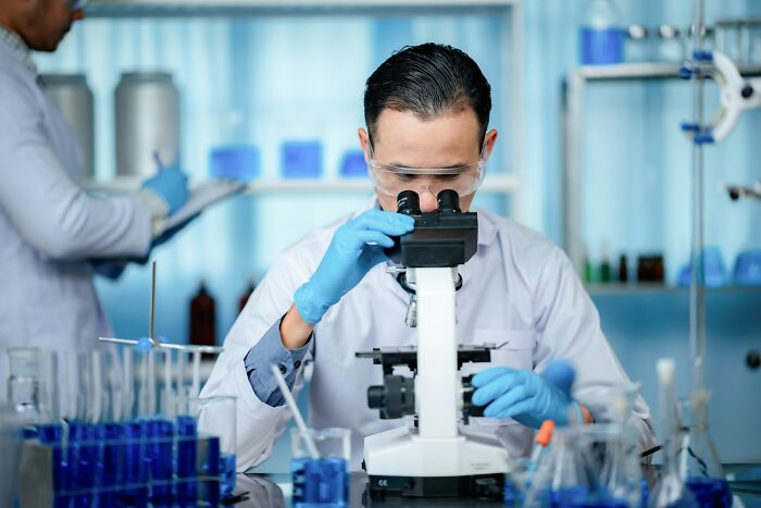 Scientist in lab wearing gloves and goggles examining samples under a microscope researching disturbing facts.