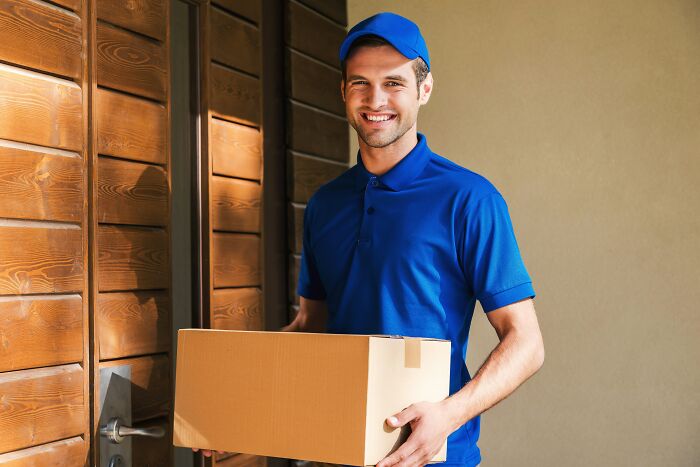Delivery worker in blue uniform holding a package, smiling at the door, showcasing unhinged hacks to land job success.