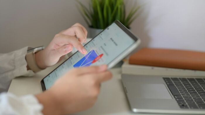 Person using a tablet to explore new facts and learning content beside a laptop on a white desk with a plant in background