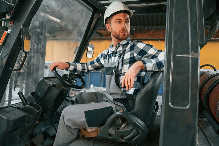 Man in a hard hat and work overalls sitting in heavy machinery, representing folks who did something NSFW and shared online.