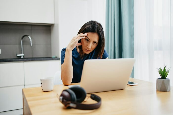 Woman in casual clothes looking confused at a laptop, experiencing glitches in the matrix while working from home.