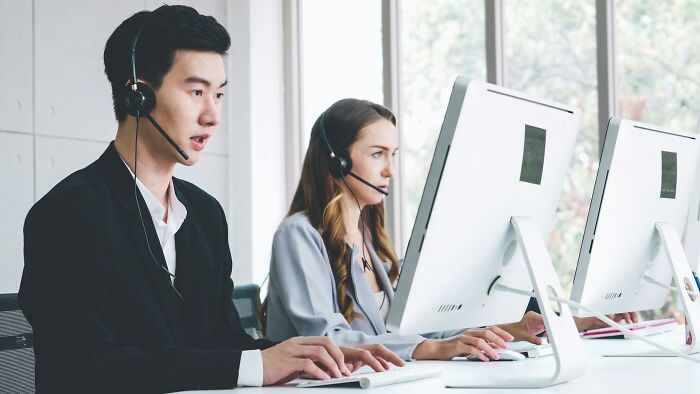 Two call center workers wearing headsets, focused on computers, representing job interview red flags in toxic workplaces.