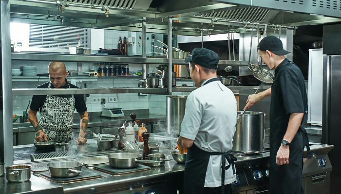 Three chefs working in a commercial kitchen with stainless steel appliances, illustrating job interview red flags.