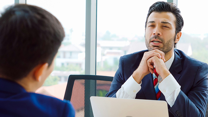 Man in a suit discussing work with colleague, symbolizing a guy expected to teach years of knowledge before PTO.