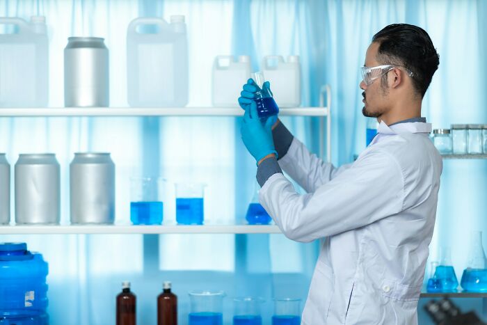Scientist in lab coat and gloves examining blue liquid in flask, representing good news in scientific research.