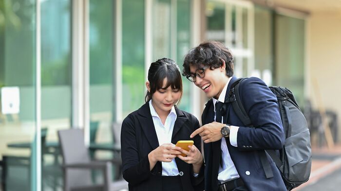 Two young professionals excitedly sharing new facts on a smartphone outside a modern office building.