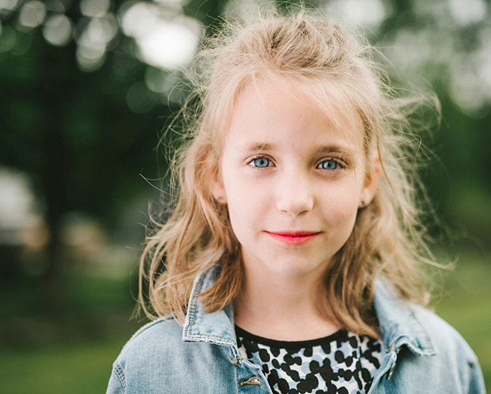 Young girl with blue eyes and messy hair standing outdoors, illustrating kindness after being bullied over a party seat. Young girl with blue eyes and messy hair standing outdoors, illustrating kindness after being bullied over a party seat.