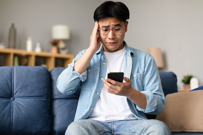 Young man looking worried while holding phone, depicting jealous boyfriend upset over girlfriend being nice to stranger.