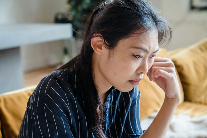 Young woman looking thoughtful indoors, reflecting on her girlfriend who got a massive tattoo recently.