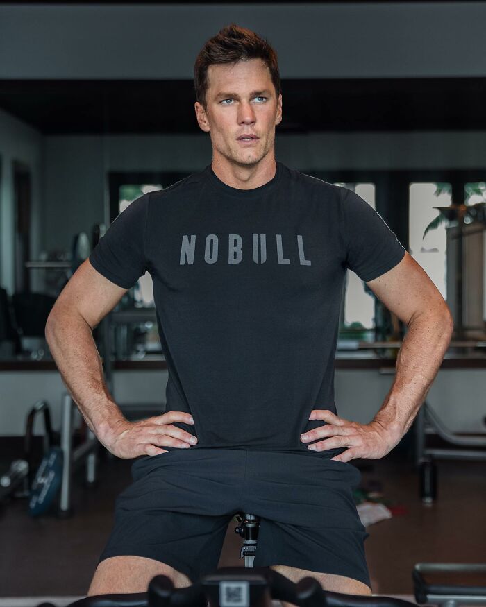 Tom Brady in a black Nobull shirt working out indoors, highlighting tensions with Gisele B&uuml;ndchen over parenting comments.