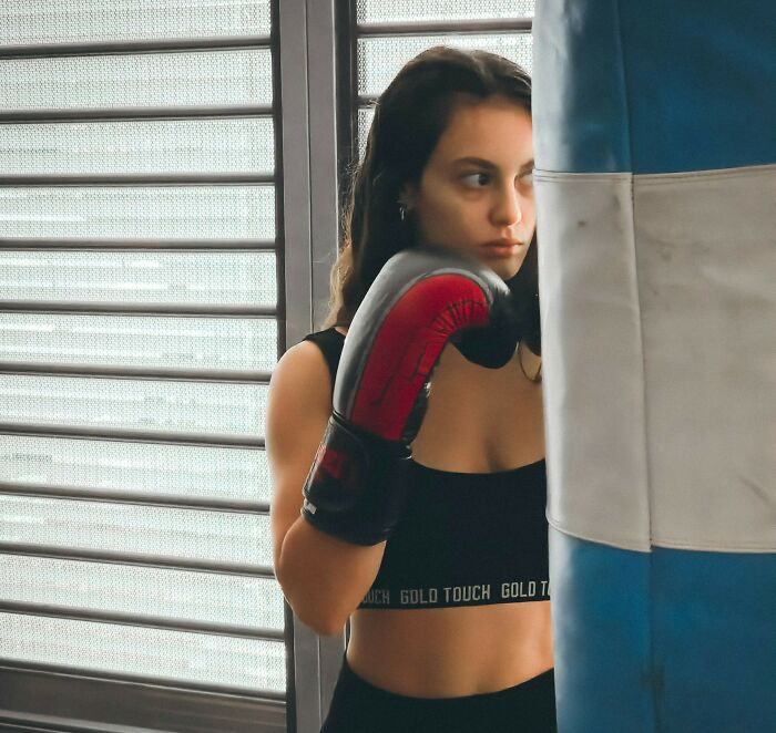 Woman wearing boxing gloves and workout clothes, punching a blue and white heavy bag in a gym.