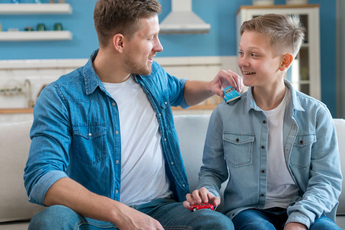 Teen boys playing with toy cars indoors, enjoying time together in a casual home setting.