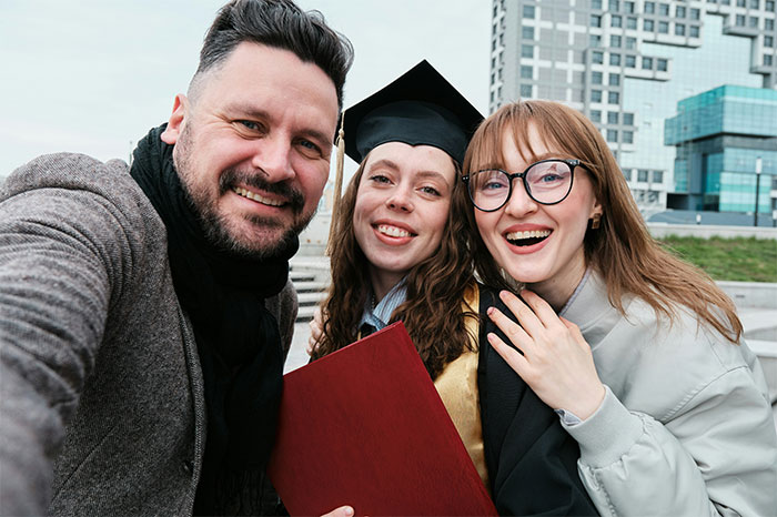 Graduate smiling in cap and gown with friends outside a city building celebrating graduation success.