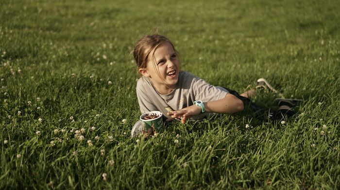 Young girl lying on grass, eating ice cream, enjoying a sunny day, illustrating glitches in the matrix experiences.