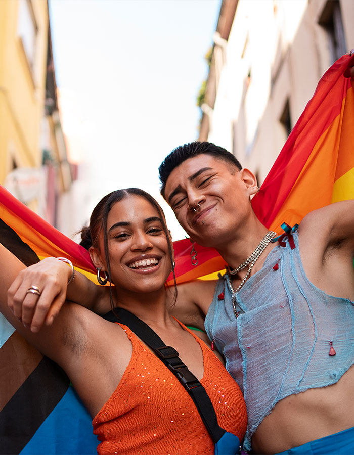 Two smiling people holding a pride flag, representing conversation around greys*xuality in modern dating culture.