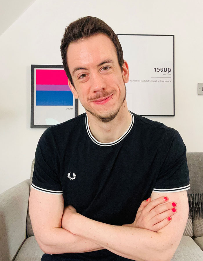 A man with short dark hair and a black shirt smiling with arms crossed, highlighting greysexuality in dating culture.
