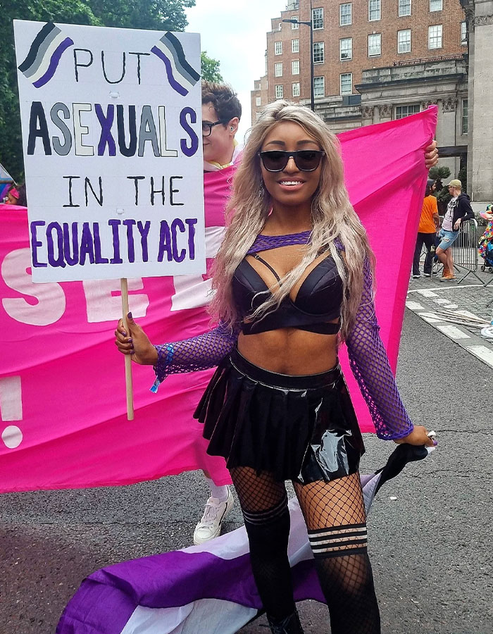Person at pride event holding sign about asexuals and equality act, highlighting greys*xuality in modern dating culture.
