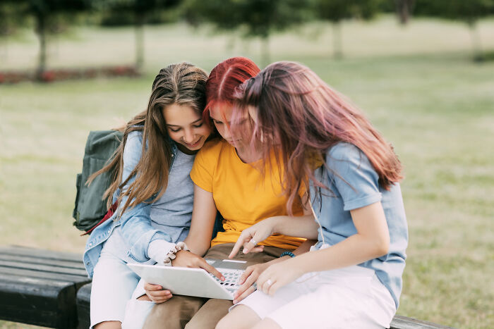 Three teenage girls closely looking at a laptop outdoors, showing reactions typical of Reddit not for the faint of heart.