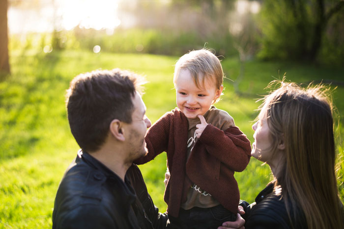 A woman and man play with a smiling toddler outdoors, highlighting autistic stepbro relationships and caregiving challenges.