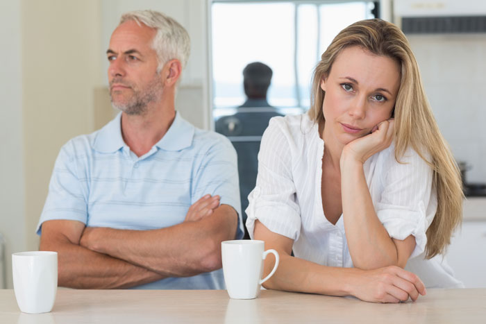 Woman refusing to be future caregiver for autistic stepbrother, sitting frustrated with man across the table in a kitchen.