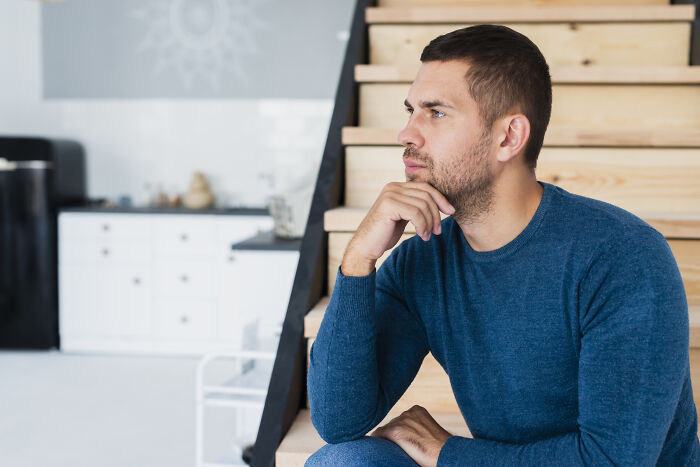 Man in a blue sweater sitting on wooden stairs, deep in thought, illustrating words that don’t exist in English but used in other languages.