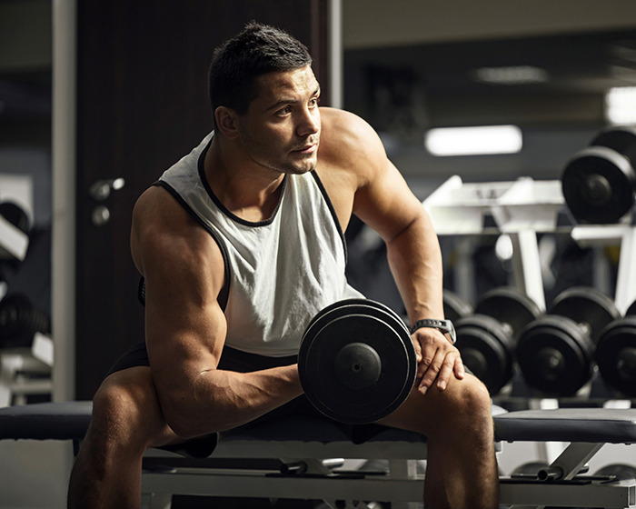 Muscular gymgoer lifting dumbbell while seated on bench in a gym, highlighting common post-workout mistakes to avoid.