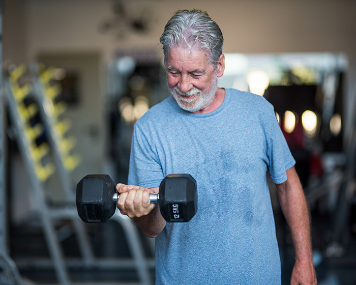 Older gymgoer lifting dumbbell in gym, highlighting common post-workout mistake and expert prevention tips.