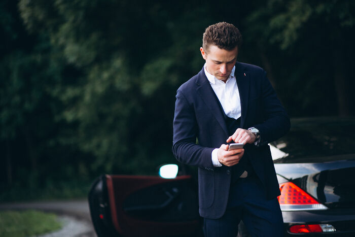 Man in suit checking watch by luxury car, illustrating wealth gap and financial contrast concepts.