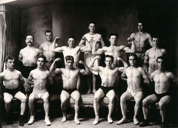 Group of handsome Victorian men posing shirtless, flexing muscles in a vintage black-and-white bodybuilding photo.