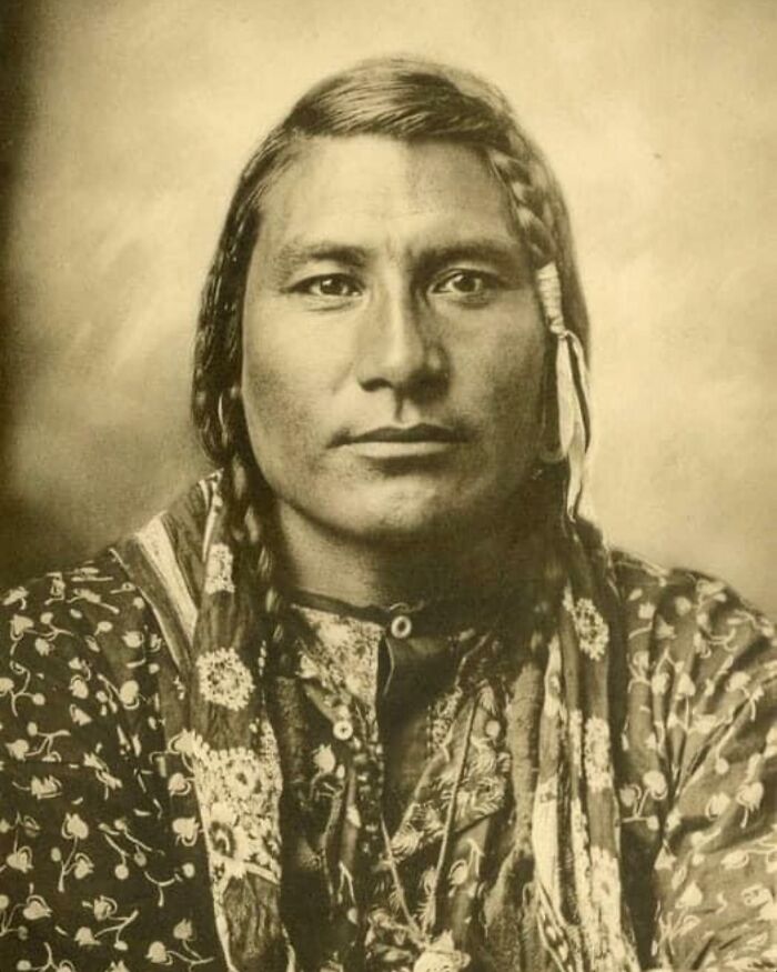 Vintage sepia portrait of a handsome Victorian man with braided hair wearing traditional patterned clothing.