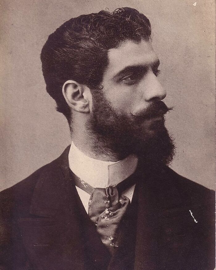 Victorian man with styled hair and full beard wearing a suit and cravat, classic handsome Victorian men portrait.